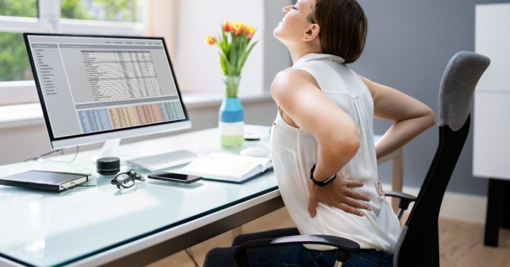 woman-holding-lower-back-in-pain-while-working-at-a-desk