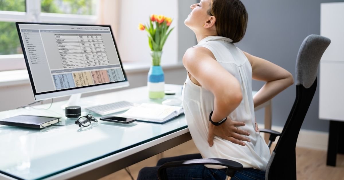 woman-holding-lower-back-in-pain-while-working-at-a-desk