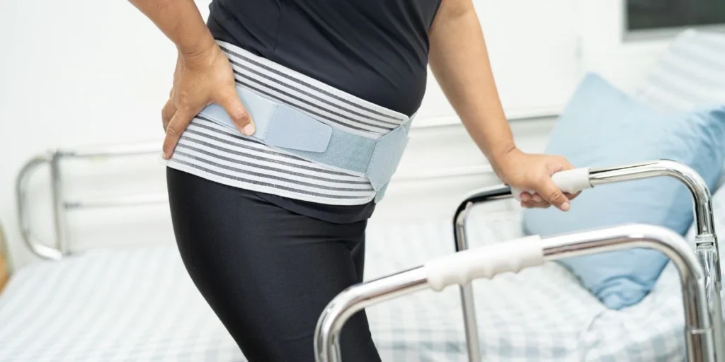 Elderly person using a walker and wearing a lumbar support belt for lower back pain relief.