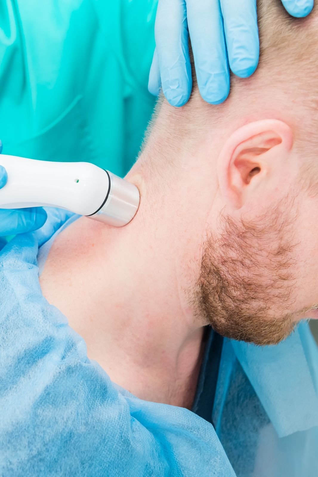 A healthcare professional in blue gloves using a laser therapy device to treat a patient's neck in a clinical setting.